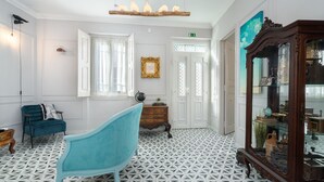 A room with a geometric patterned floor, a blue armchair, a wooden cabinet with glass doors, and a door with a green exit sign. - ♥ Unique & Stylish Historic House ♥ Great Location ♥ Close to Gardens & River (Leiria)