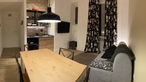 Una cocina moderna con una mesa y sillas de madera, una lámpara colgante negra y una zona de comedor con sofá.