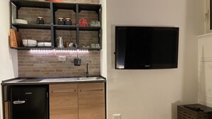 Una cocina compacta con refrigerador empotrado, un lavamanos y un televisor montado en la pared.