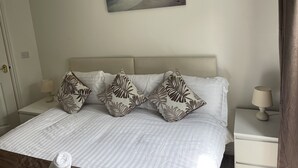 Un dormitorio con cama, almohadas, una mesita de noche, una lámpara y un cuadro de una playa.
