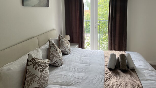 Un dormitorio con cama, almohadas, un cuadro y vistas al balcón.