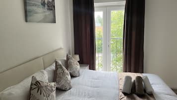 A bedroom with a bed, pillows, a painting, and a balcony view.