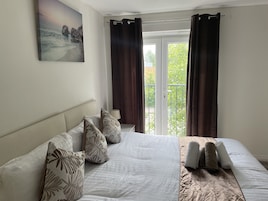Quarto com cama, almofadas, um quadro e vista para a varanda.