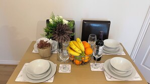 Una mesa de comedor dispuesta con platos, vasos, una cesta de fruta, una botella de vino y plantas decorativas.