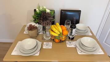 A dining table set with plates, glasses, a fruit basket, a wine bottle, and decorative plants.
