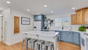 A modern kitchen with a central island, bar stools, blue cabinets, and a white refrigerator.