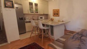 A compact kitchen with white cabinets, a microwave, and a dining area with white chairs.