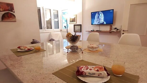 A dining area with a table set for two, a bowl of fruit, and a snack package.