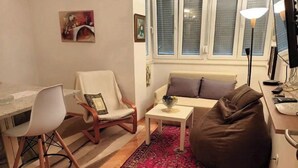 A living room with a sofa, a chair, a small table, a rug, and a window with blinds.