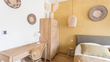 Un dormitorio con un escritorio de madera, una silla, un armario, una cama con cabecera gris y dos lámparas de pared.