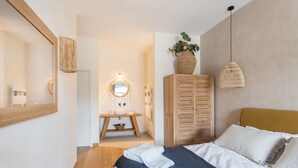 Un dormitorio con cama, un armario de madera, un espejo, una lámpara colgante y una planta.