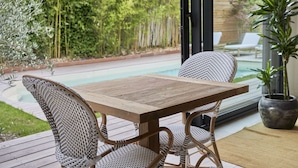 Una mesa de madera con sillas de mimbre en un patio con vista a la piscina.