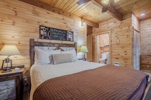 A wooden cabin-style bedroom with a bed, bedside lamps, a wall-mounted quote, and a ceiling fan. - Lakefront 4BR/4BA Cabin with Sauna, Hot Tub & Private Dock – Minutes from YNP! (Island Park)