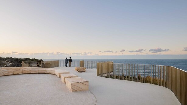 Une terrasse au bord de l’eau, dotée d’une plateforme en bois aux lignes courbes, d’espaces aménagés pour s’asseoir et d’une rambarde offrant une vue sur la mer.