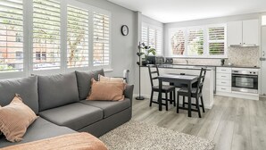 Une cuisine moderne avec des meubles blancs, un coin repas comprenant une table et des chaises, et un canapé gris agrémenté de coussins.