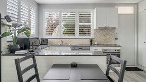 Une cuisine moderne avec des meubles blancs, un plan de travail noir et une fenêtre équipée de stores.