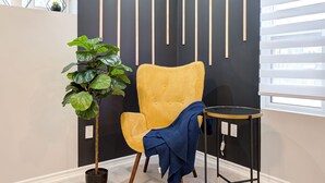Una habitación con un sillón amarillo, una planta en maceta, una mesita redonda y una pared con listones de madera verticales.