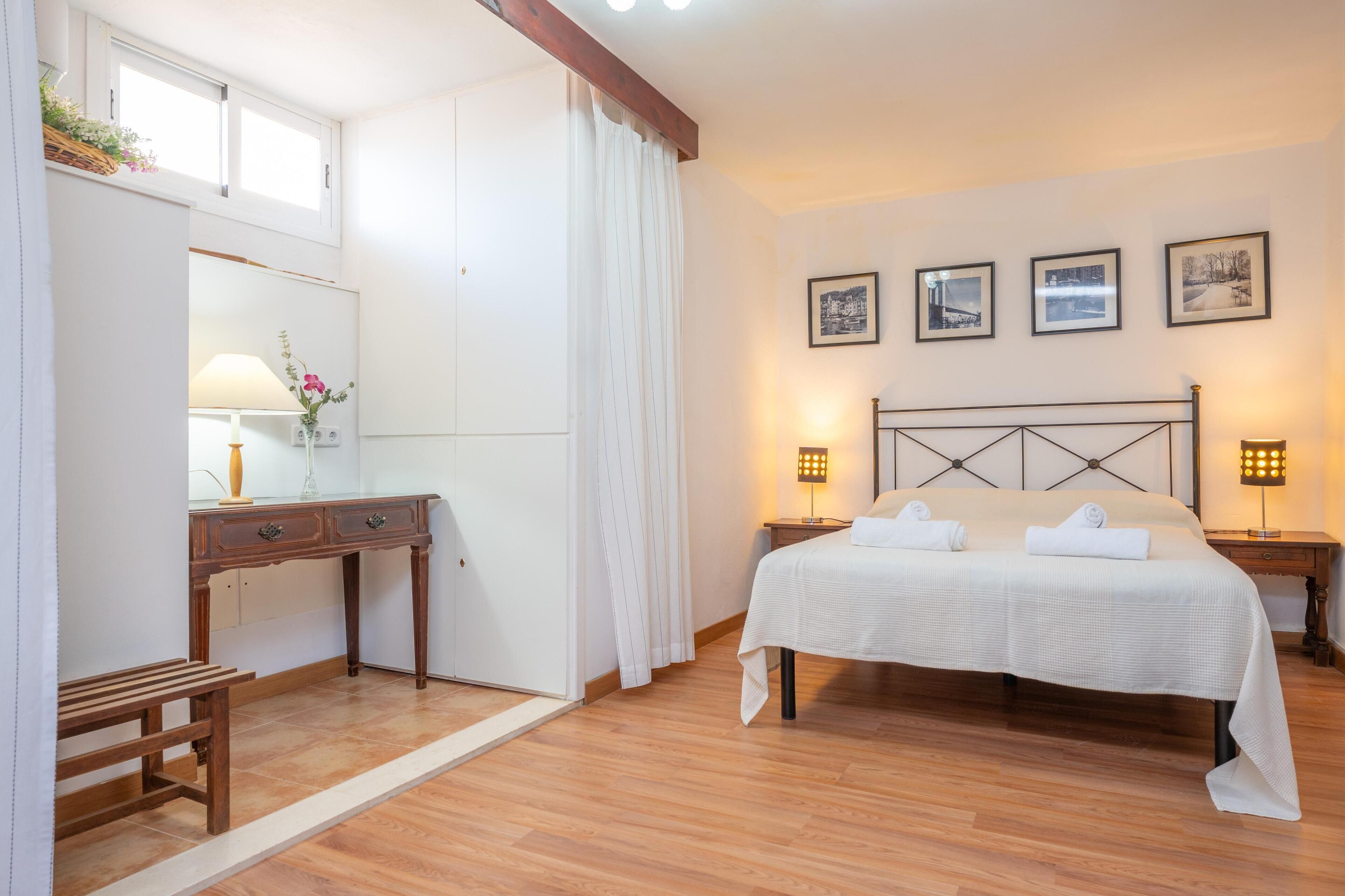 Un dormitorio con cama, mesitas de noche, un escritorio, una silla y una ventana con cortinas.