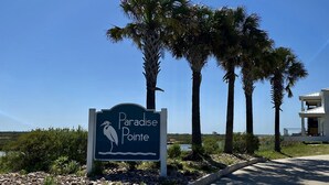 A sign for Paradise Pointe with a bird silhouette, surrounded by palm trees and a clear sky. - New Listing in Paradise Point Community (Port Aransas)