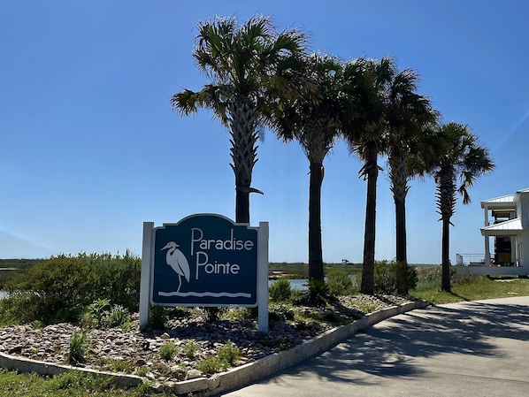 A sign for Paradise Pointe with a bird silhouette, surrounded by palm trees and a clear sky.