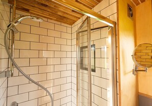 Bathroom features a shower area with a glass door, large square tiles, and a wooden ceiling with exposed beams.