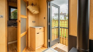 A compact room with a wooden interior, a small kitchenette, a door leading to a balcony, and a large black cylindrical object.