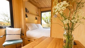 A cozy room with a wooden bed, a small table, and a chair. There's a vase with flowers on the table.