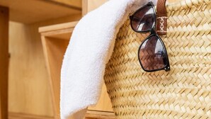 A woven bag, a pair of sandals, and a pair of sunglasses on a wooden floor.