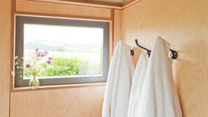 A bathroom with wooden walls, a window with a view of greenery, and two white towels hanging on a hook. - A secluded, design-led shepherd’s hut for slow, off-grid stays by the coast (Cardigan)