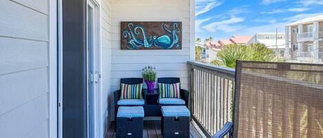 A balcony with two wicker chairs, a small table, and a colorful cushion.