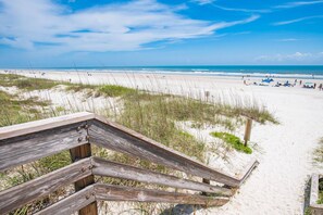 A wooden boardwalk leading to a sandy beach with dunes and a clear blue sky. - Butler Beach Bungalow (St. Augustine)