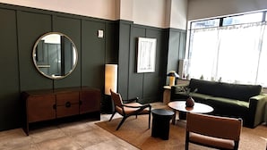 A room with a dark green wall, a round mirror, a sofa, two chairs, a small table, and a window with curtains. - Dutch Hotel Long Island City New York , Belvilla District 6 Formerly Sonder  (Long Island City)