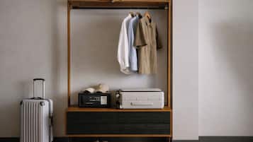 A wooden wardrobe with hanging clothes, a suitcase, a radio, and a pair of shoes.