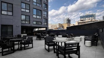 An outdoor seating area with tables and chairs, a modern building in the background, and a clear sky.