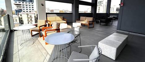 Una terraza en la azotea con mobiliario exterior, una mesa redonda y vistas a la ciudad.