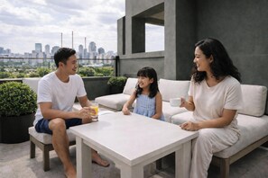 Eine dreiköpfige Familie auf einer Dachterrasse mit Blick auf eine Stadtlandschaft.
