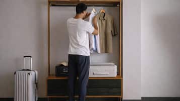 Una persona ordenando ropa en un armario de madera, una maleta y una impresora sobre una mesa de madera.