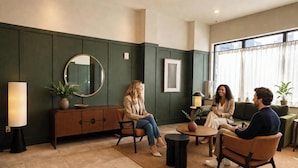 A modern interior with a seating area, a round mirror, a framed picture, and a large window. - Dutch Hotel Long Island City New York , Belvilla District 6 Formerly Sonder  (Long Island City)
