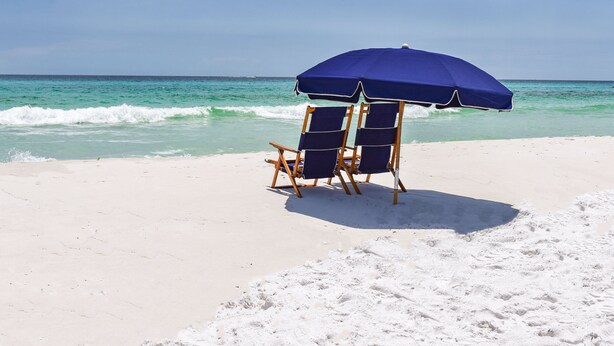 A beach scene with two blue beach chairs and a blue umbrella on the sand. - Crystal Beach Dream with Pool, Dog Park, and Beach Access (Destin)
