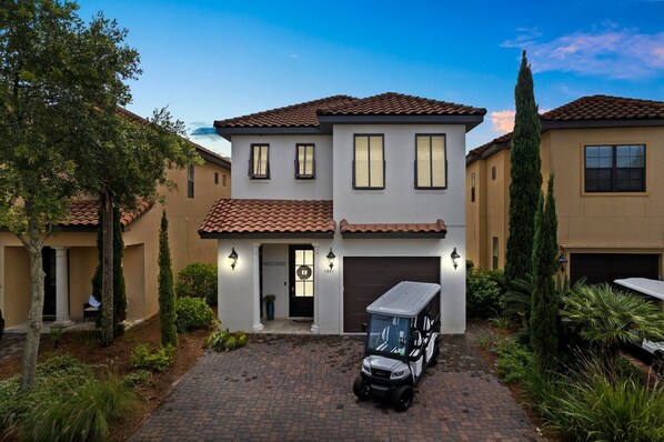 A two-story house with a garage, a driveway, and a golf cart parked in front. - Venetian Boardwalk with Low-Speed Vehicle, Pool, and Waterfront Views (Miramar Beach)