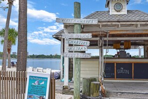 A wooden signpost with directions to various activities like 'Waverunners,' 'Tree House,' 'Charters,' 'Kayaks,' and 'Village.' - Venetian Boardwalk with Low-Speed Vehicle, Pool, and Waterfront Views (Miramar Beach)