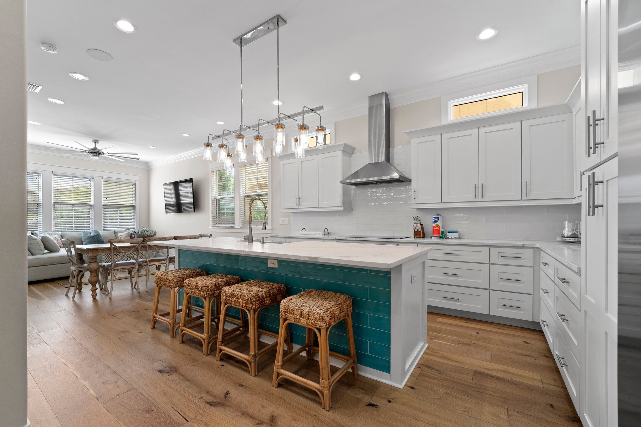 Una cocina moderna con armarios blancos, salpicadero verde azulado y taburetes de madera.