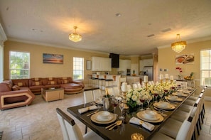 A dining area with a long table set for a meal, a sofa, and a kitchen in the background.