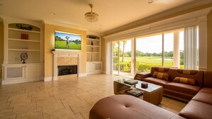 A living room with a fireplace, television, and a view of a golf course. - THE GOLF COURSE HOUSE, pet friendly, mini home theater, sleeps 18 (reunion)