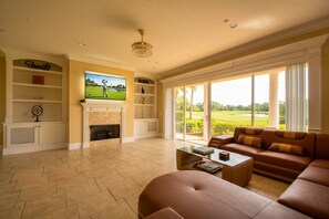 Una sala de estar con chimenea, televisión y vista a un campo de golf.