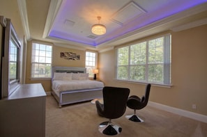 A bedroom with a bed, two chairs, a dresser, and large windows.