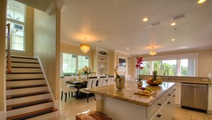 A kitchen with a central island, a dining area with chairs, a staircase, and a view of the outdoors. - THE GOLF COURSE HOUSE, pet friendly, mini home theater, sleeps 18 (reunion)