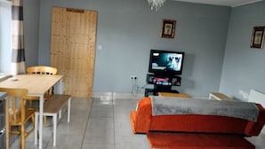 A living room with a wooden door, a television, a sofa, and a dining table with chairs.
