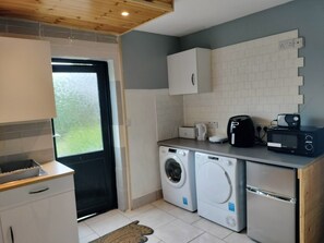 A compact kitchen with a washing machine, a microwave, a toaster, and a coffee maker. - One Bedroom Apartment Achill Island Pets Allowed (Achill Island)