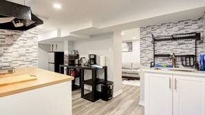 A modern kitchen with a central island, a built-in oven, and a black range hood. There is a dining area with a wooden table and chairs, and a living room with a sofa and a coffee table. - 1 Bedroom Apartment Downtown - Close to Hospital and University  (Kitchener)